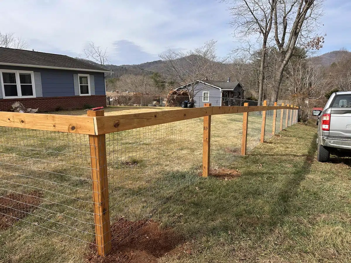 Hog wire fence installation with wooden posts in a residential yard in Asheville,